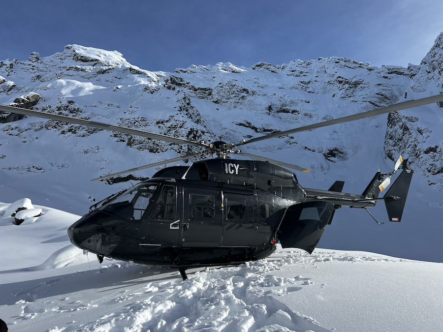 Black Kawasaki BK117 helicopter landed on a Glacier, perfect for private charters and group adventures.